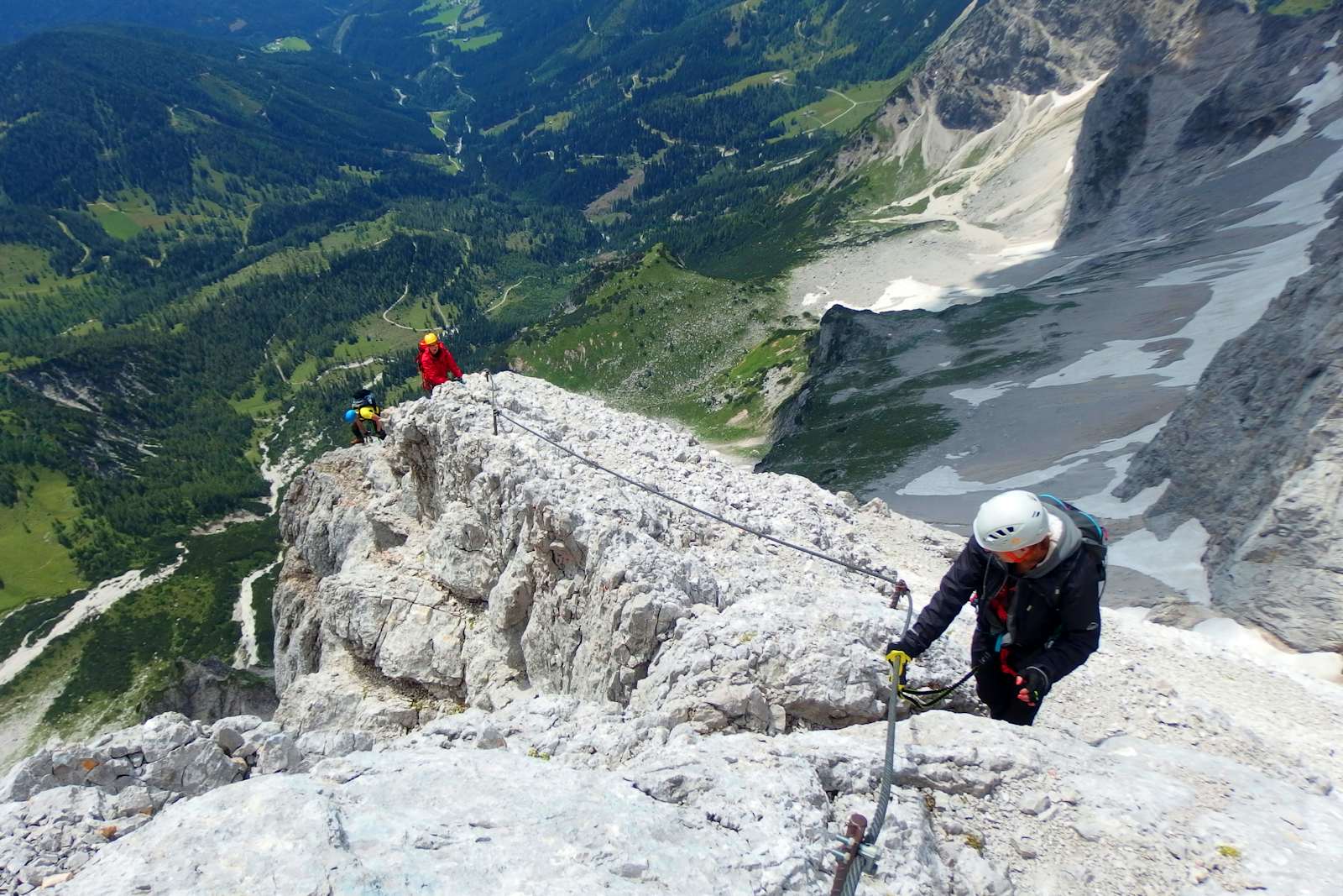Person in a helmet clipped to the steel cable of a via ferrata above a valley